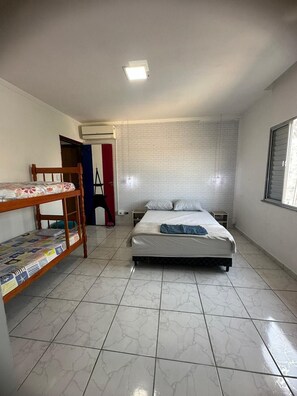 A room with a bunk bed, a single bed, a small table, and a window. - Casa Paraíso em Família - Praia Grande (Praia Grande)