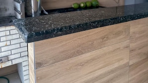 A kitchen with a wooden backsplash, a black countertop, and a stainless steel sink.