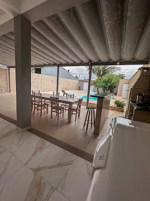 Un patio exterior con mesa y sillas, piscina y zona de barbacoa.