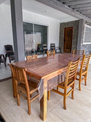 A large wooden dining table with chairs, a glass partition, and a stone wall. - Casa Paraíso em Família - Praia Grande (Praia Grande)
