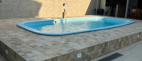 A swimming pool with a tiled deck, a brick wall, and a covered patio area.