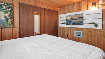 A wooden-paneled room with a bed, a welcome sign, a painting, and a thermostat.