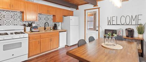Una cocina moderna con armarios de madera, un refrigerador blanco y una zona de comedor con mesa y sillas de madera.