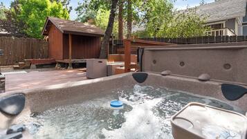 A hot tub with a wooden deck and a wooden structure in the background.