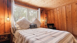 Ein gemütliches Schlafzimmer mit Bett, Kissen, einem Nachttisch und einem Fenster mit Jalousien.