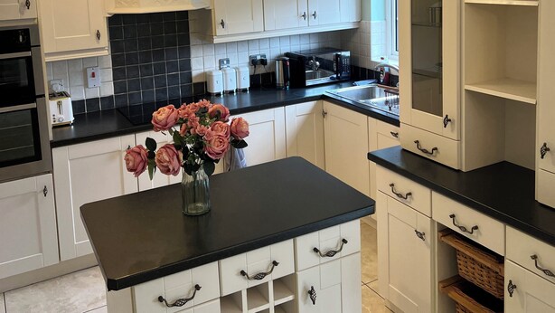 Eine moderne Küche mit weißen Schränken, einer schwarzen Arbeitsplatte und einem Blumenstrauß in Rosa auf der Kücheninsel.