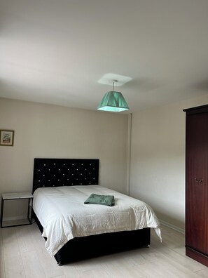 A bedroom with a bed, a bedside table, a wardrobe, and a hanging light fixture.