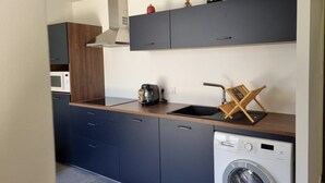A compact kitchen with dark cabinets, a wooden countertop, a built-in washing machine, and a microwave. - Quiet apartment in a green setting (Nîmes)