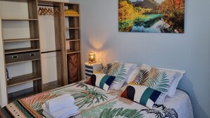 A bedroom with a bed, a nightstand, a lamp, a wardrobe, and a painting of a landscape. - Quiet apartment in a green setting (Nîmes)