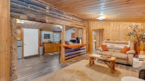Interior de una cabaña de troncos con cocina, comedor y sala de estar.