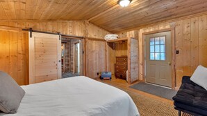 Un dormitorio de cabaña de madera con cama, cómoda y puerta corredera.