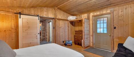 A wooden cabin bedroom with a bed, dresser, and a sliding door.
