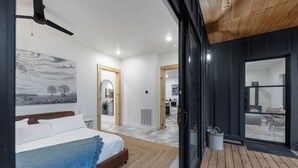 Una camera da letto moderna con un letto, soffitto in legno e vista sull'area soggiorno attraverso una porta in vetro.