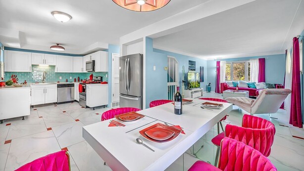 Une cuisine moderne avec des meubles blancs, un îlot central et un coin repas avec des chaises rouges.