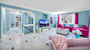 Un salon spacieux avec une grande télévision, un canapé rose et un escalier menant à un autre niveau.