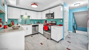 Une cuisine moderne avec des meubles blancs, un four à micro-ondes, un lave-vaisselle et un four rouge.