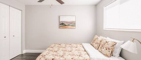 A bedroom with a bed, a ceiling fan, a window with blinds, and a framed picture on the wall.