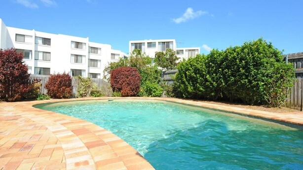 Una piscina con borde de baldosas, rodeada de vegetación y edificios modernos.