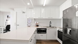 A modern kitchen with white cabinetry, a stainless steel refrigerator, a microwave, and a stove. - Lindomare Unit 10, 11 Orvieto Tce, Kings Beach (Kings Beach)