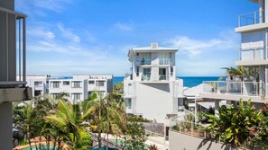 A modern building with a pool and palm trees, overlooking the ocean.