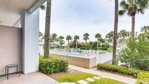 A patio area with a concrete bench, a tiled table, and a view of a swimming pool with a white fence and palm trees. - Steps to Beach, Heated Pool steps from condo! (Santa Rosa Beach)