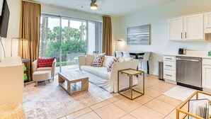 A modern living room with a sofa, coffee table, and a dining area with a table and chairs. There is a kitchen with cabinets and a dishwasher. - Steps to Beach, Heated Pool steps from condo! (Santa Rosa Beach)