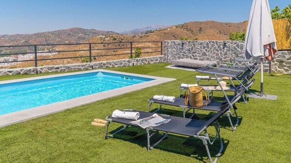 A poolside area with a stone wall, a pool, and lounge chairs with towels and a basket.
