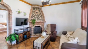 Een woonkamer met een stenen open haard, een televisie, een bank en een fauteuil.