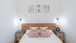 Een keurig opgemaakt slaapkamer met een houten hoofdbord, twee nachtkastjes en drie aan de muur hangende kunstwerken met abstracte figuren.