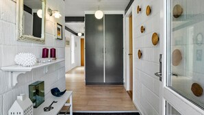 A hallway with a white brick wall, a mirror, a shelf with decorative items, and a door with wooden knobs. - 2 bedroom beautiful home in Jerup (Jerup)