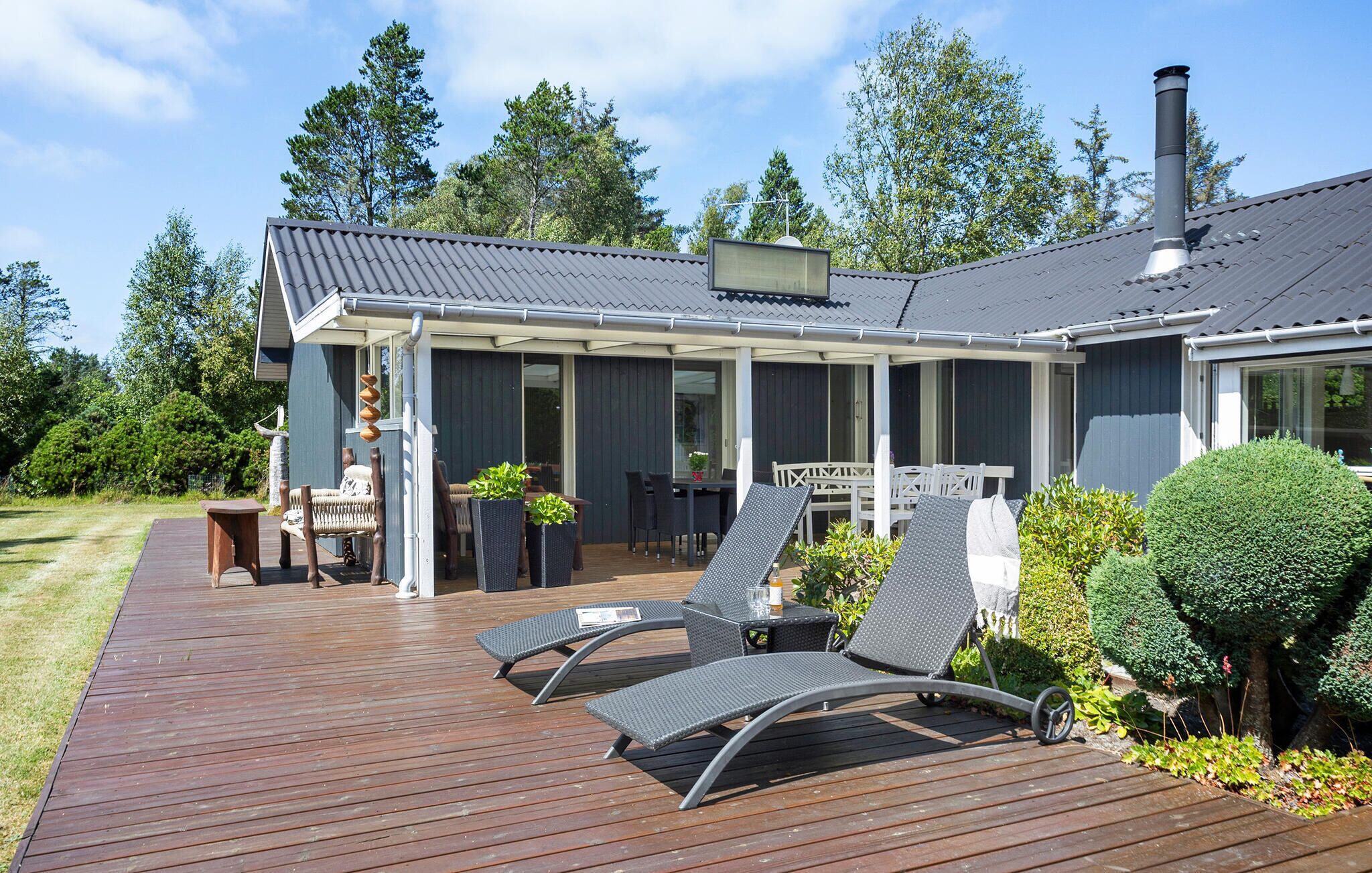 Une terrasse couverte, aménagée avec du mobilier d’extérieur, un coin repas et une cheminée.
