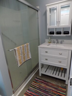 A bathroom with a glass shower door, a white sink with a mirror above it, and a striped rug on the floor. - Lady Pilot, Old North Columbus - Lovely 3-bedroom home, steps to OSU! (Columbus)