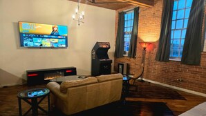 A cozy living room with a flat-screen TV, a retro arcade machine, a comfortable sofa, and a small coffee table.
