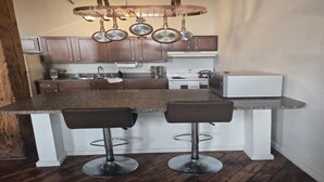 A kitchen with a granite countertop, stainless steel appliances, and hanging pots.