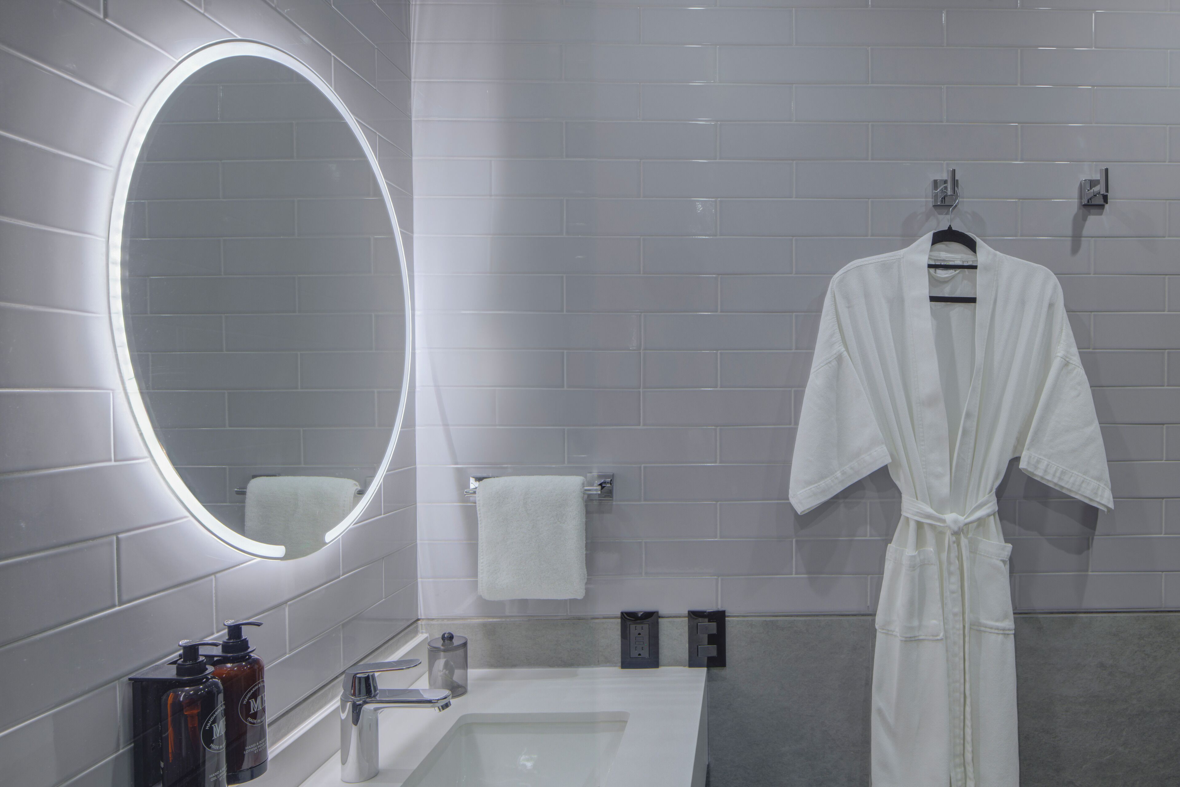 Un baño moderno con un espejo grande, una bañera blanca y una bata colgada en un perchero.