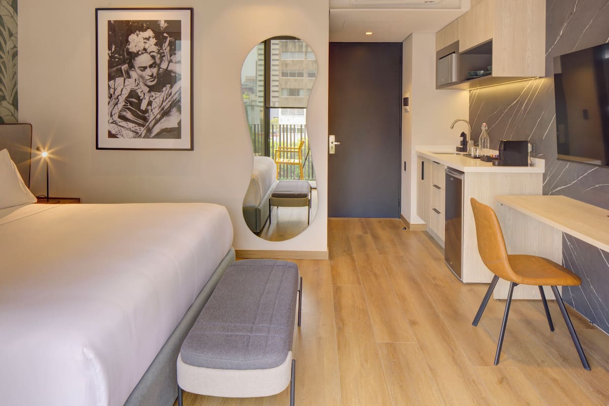Una habitación de hotel moderna con cama, una banca, escritorio y kitchenette.