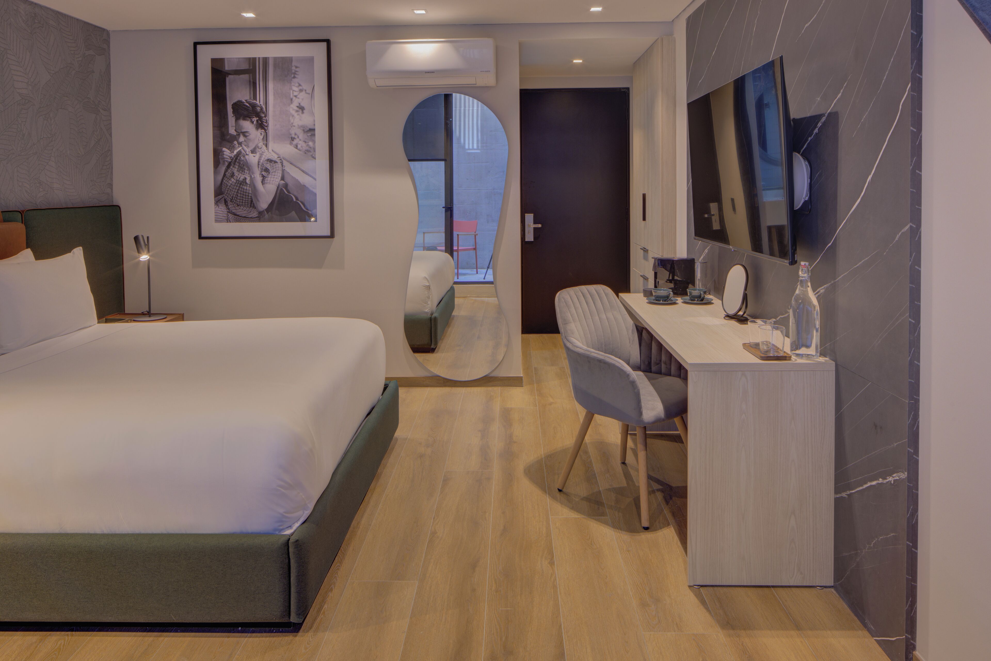 Ein modernes Hotelzimmer mit einem großen Bett, einem Schreibtisch mit Stuhl, einem Fernseher und einem gerahmten Bild an der Wand.
