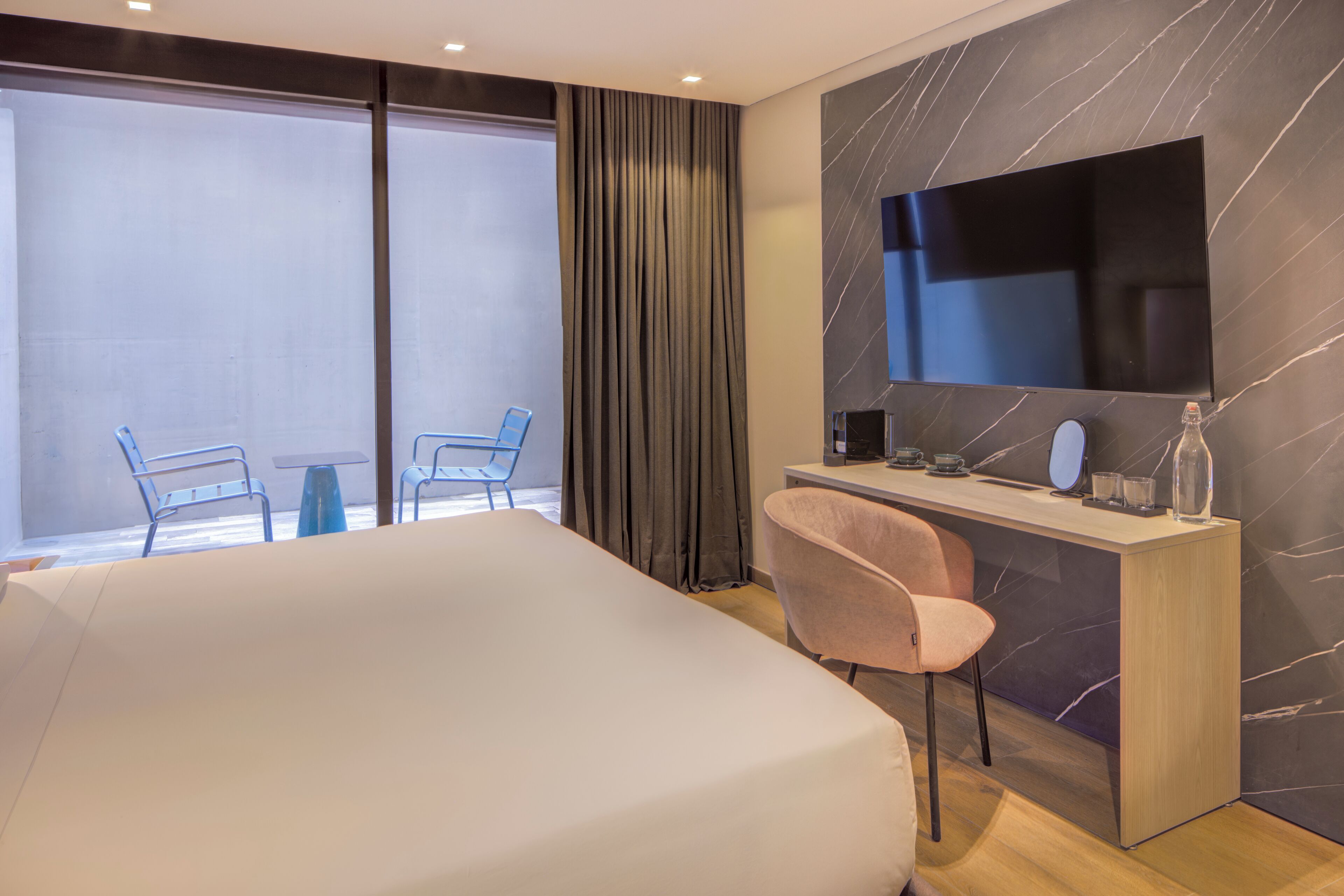 Une chambre d’hôtel avec un lit, un bureau et une chaise, une télévision et une vue sur l’extérieur.