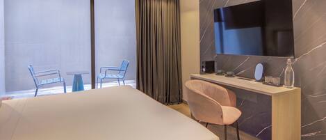 Une chambre d’hôtel avec un lit, un bureau et une chaise, une télévision et une vue sur l’extérieur.