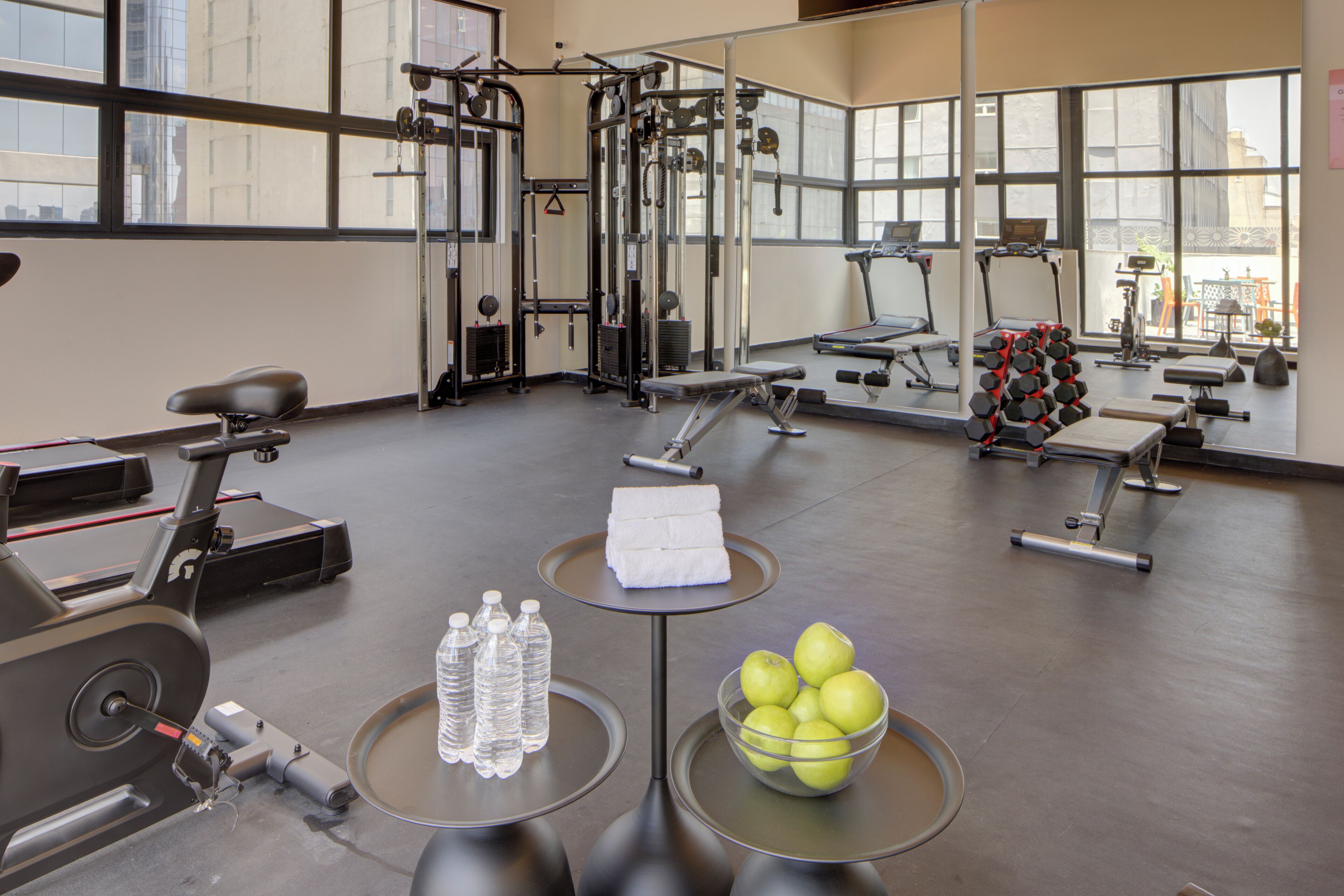 A gym with exercise equipment, water bottles, and a bowl of apples.