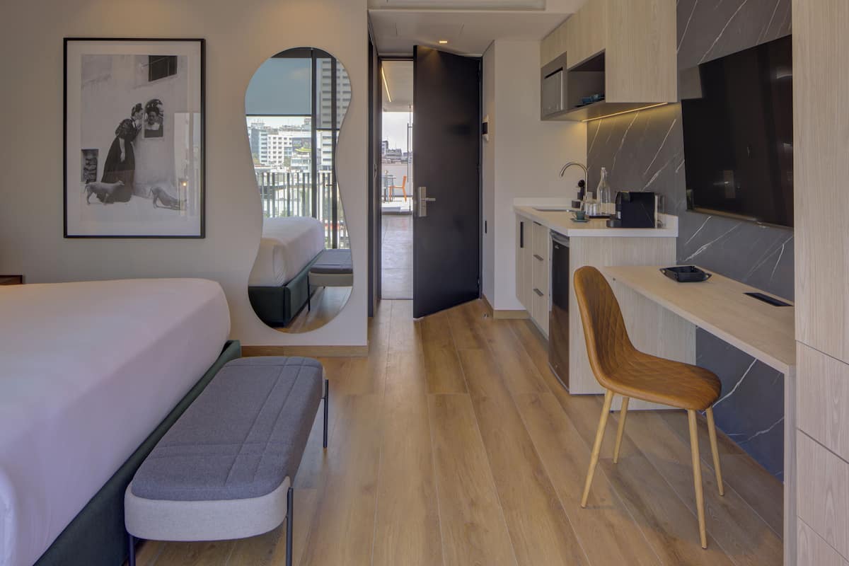 Una habitación de hotel moderna con cama, banco, escritorio y televisor.
