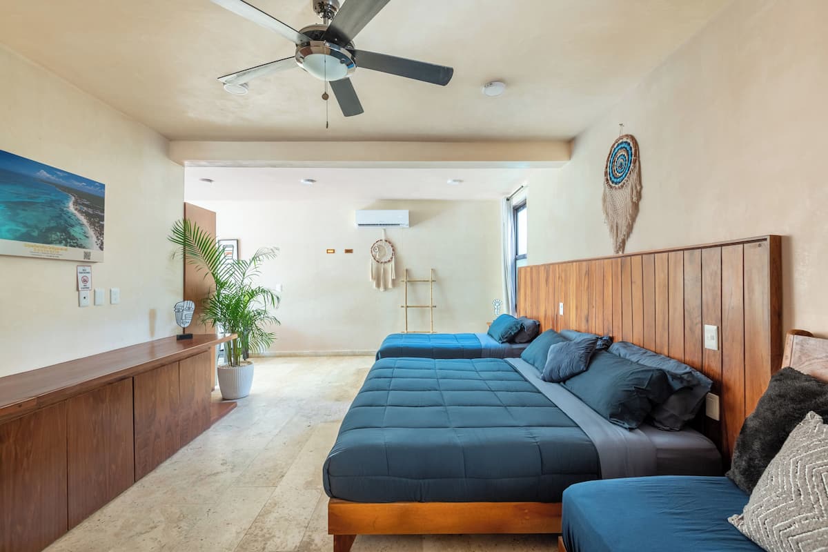 Una habitación con cama, escritorio, ventilador de techo, aire acondicionado de pared y un amplio ventanal.