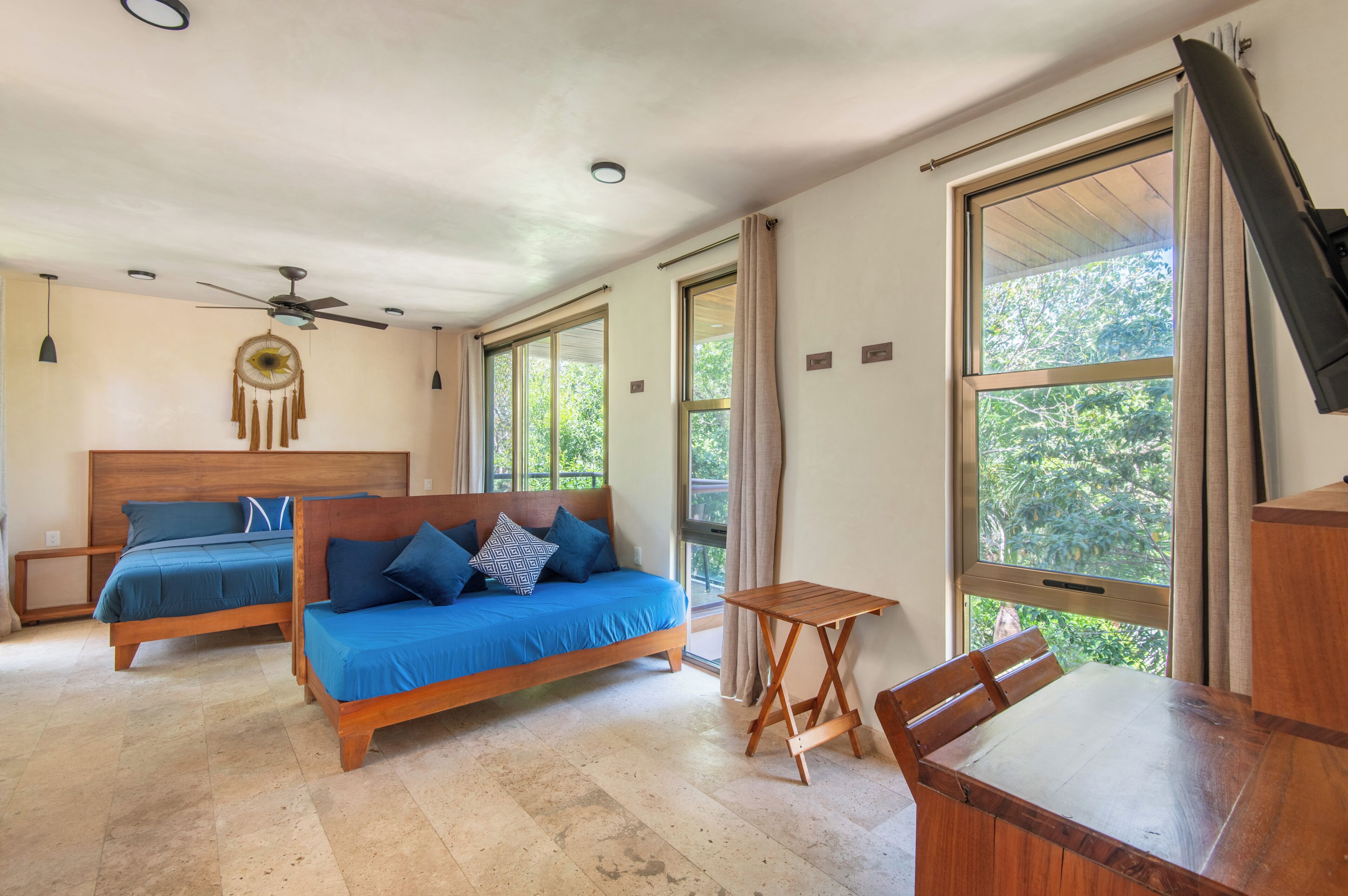 Ein Schlafzimmer mit zwei hölzernen Betten, einem Deckenventilator und großen Fenstern mit Vorhängen.