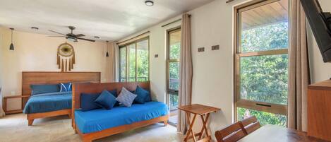 Ein Schlafzimmer mit zwei hölzernen Betten, einem Deckenventilator und großen Fenstern mit Vorhängen.