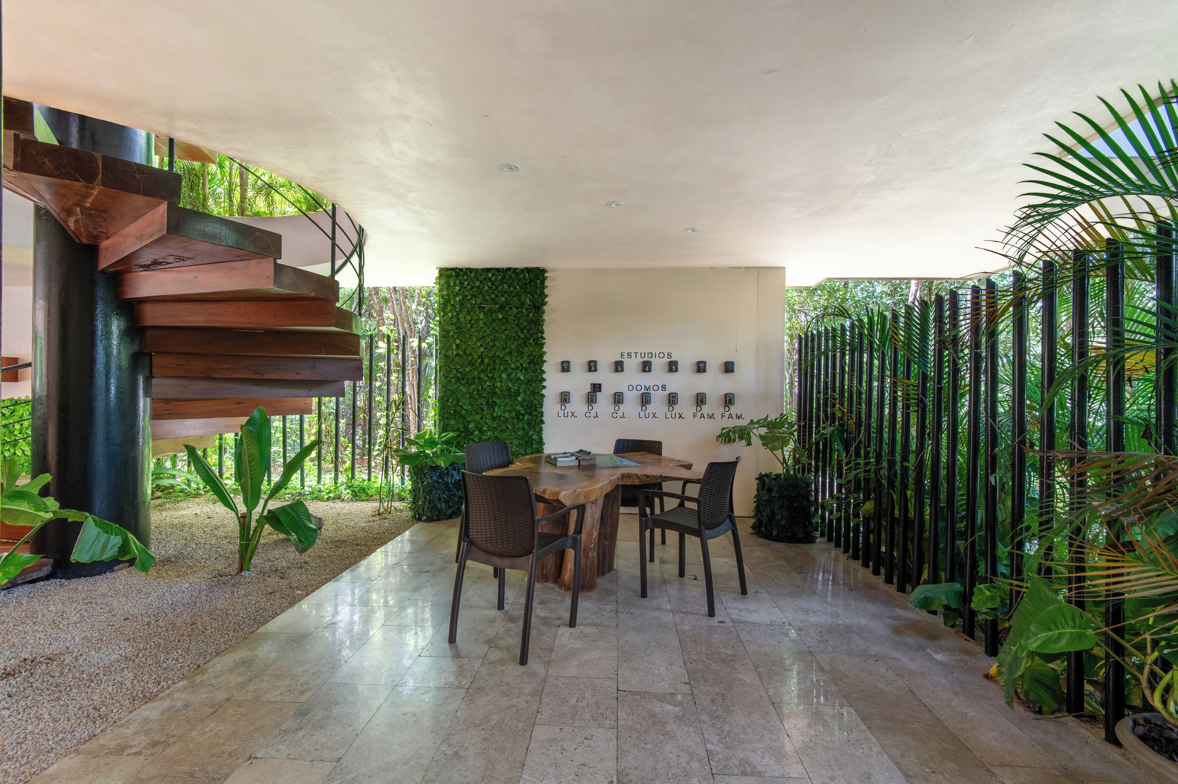 Un interior moderno con una escalera, una mesa de madera con sillas y una pared con objetos enmarcados.