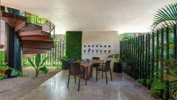 Un interior moderno con una escalera, una mesa de madera con sillas y una pared con objetos enmarcados.
