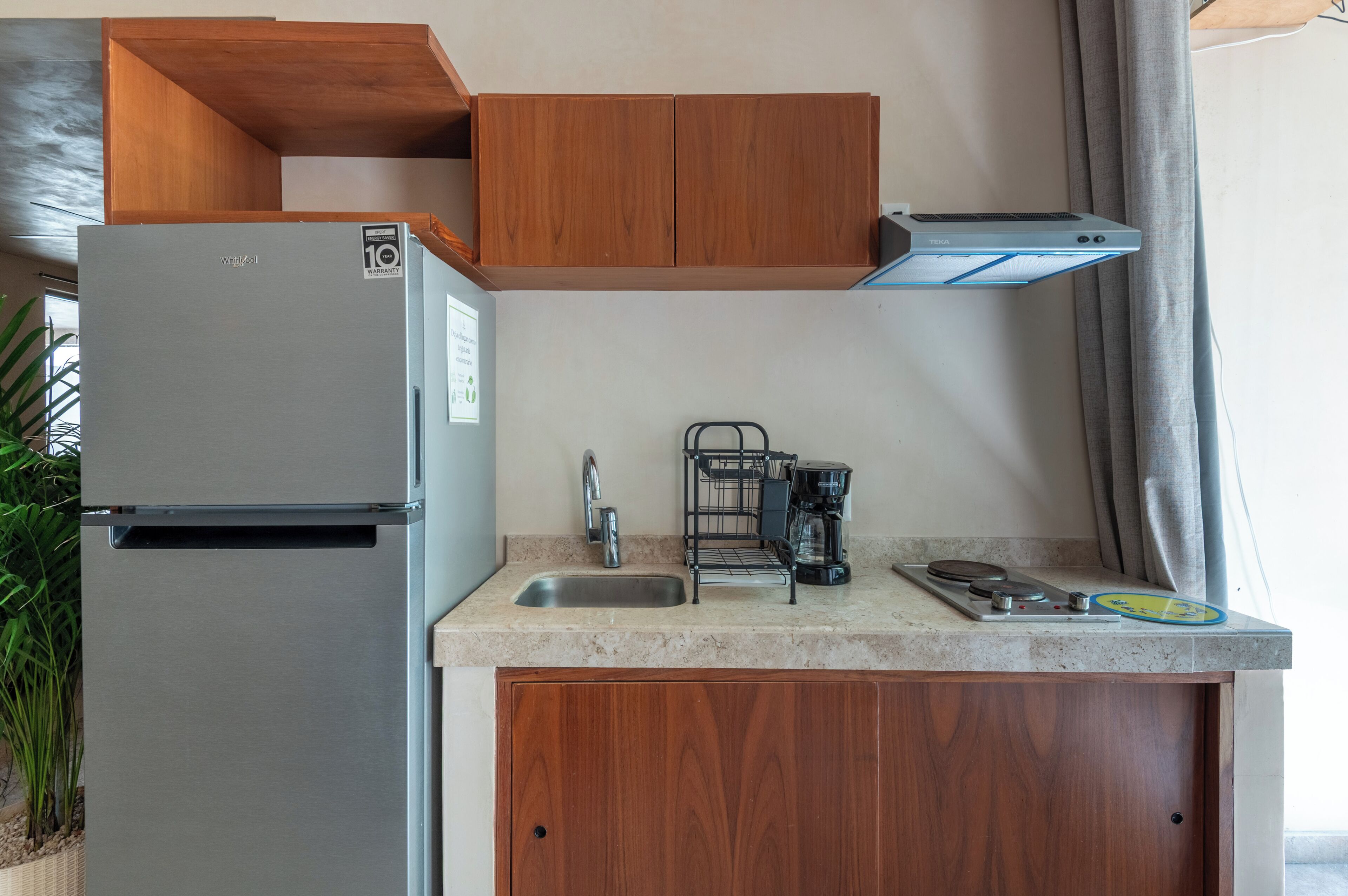 Una cocina compacta con un refrigerador de acero inoxidable, cafetera y lavabo.