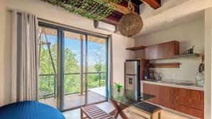 A modern kitchen with a glass table, wooden cabinets, and a view of greenery outside. - Santuario Apartments (Tulum)