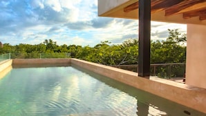 A swimming pool with a view of trees and a cloudy sky. - Santuario Apartments (Tulum)