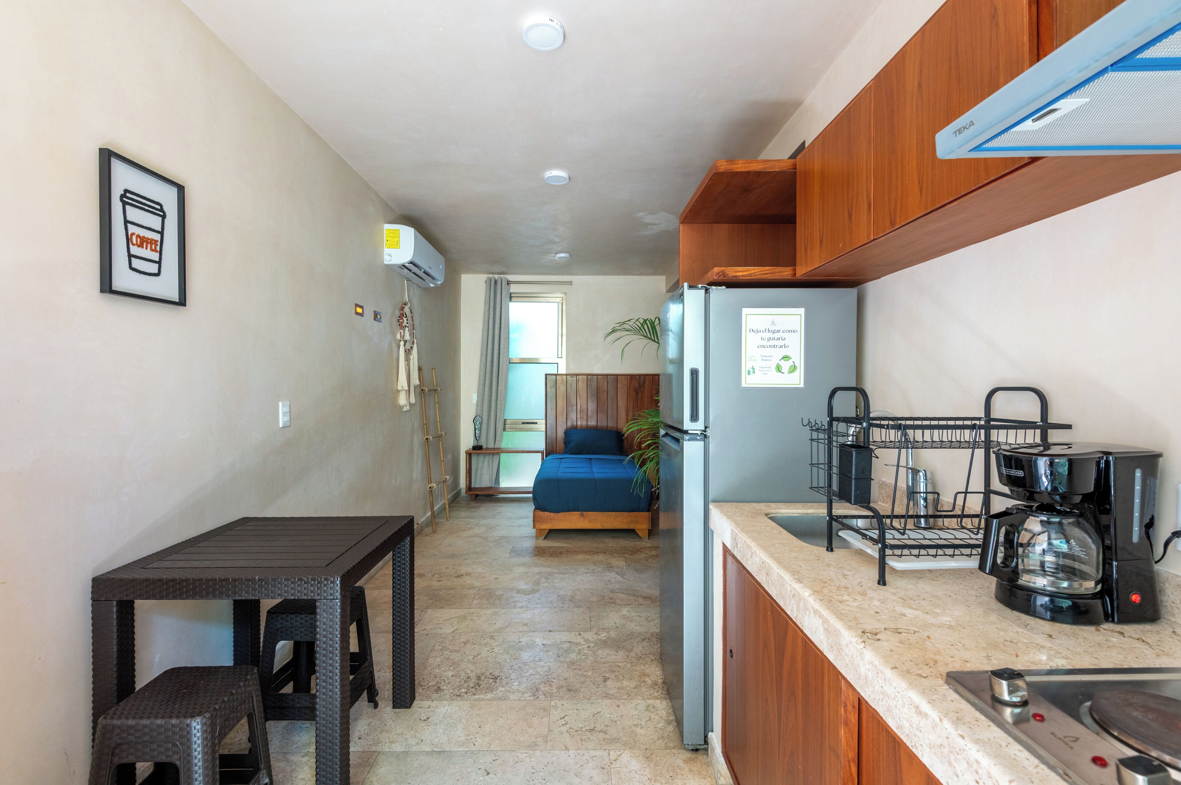 Una cocina compacta con refrigerador, cafetera y lavamanos.